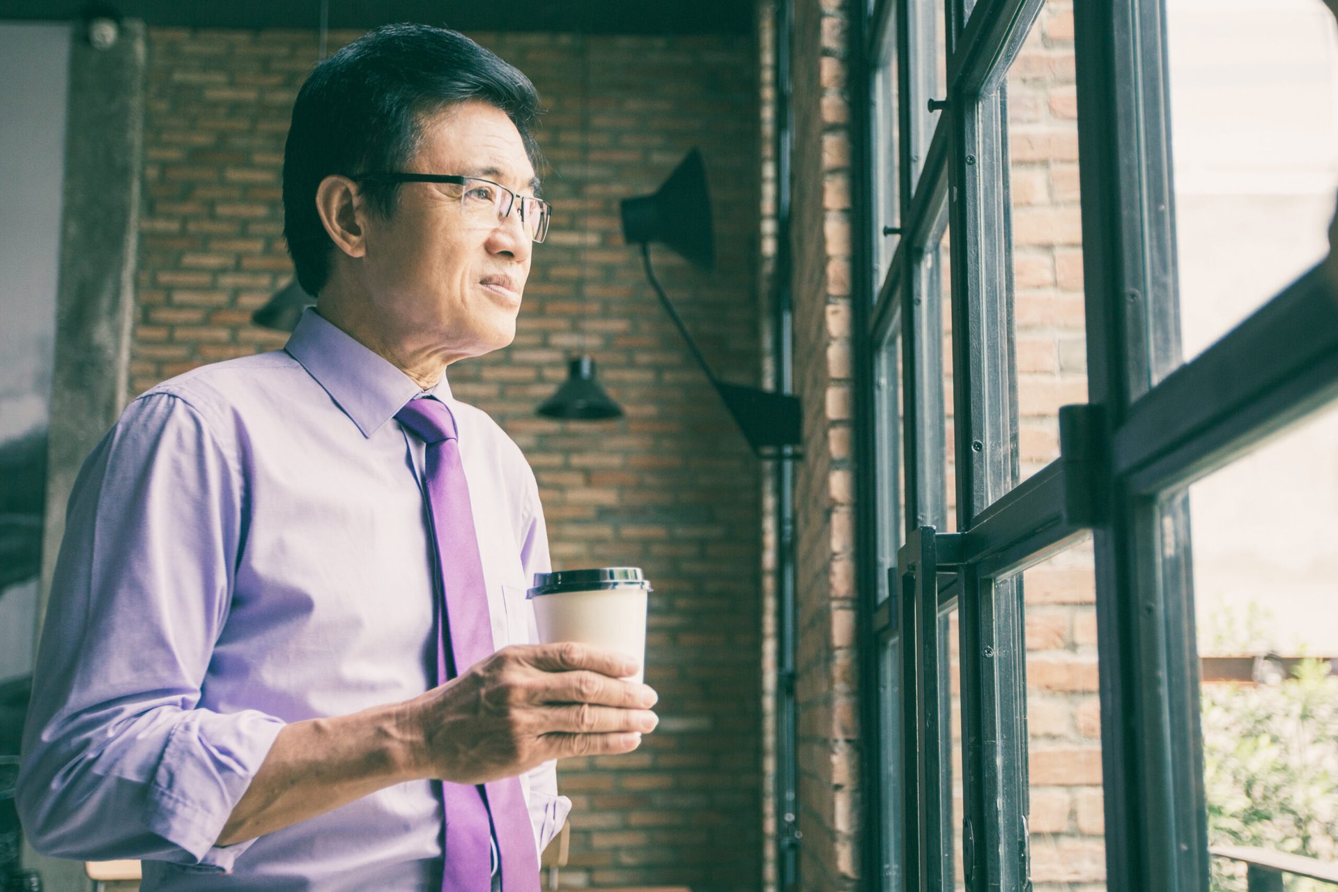 Senior male worker drinking coffee and staring out the window