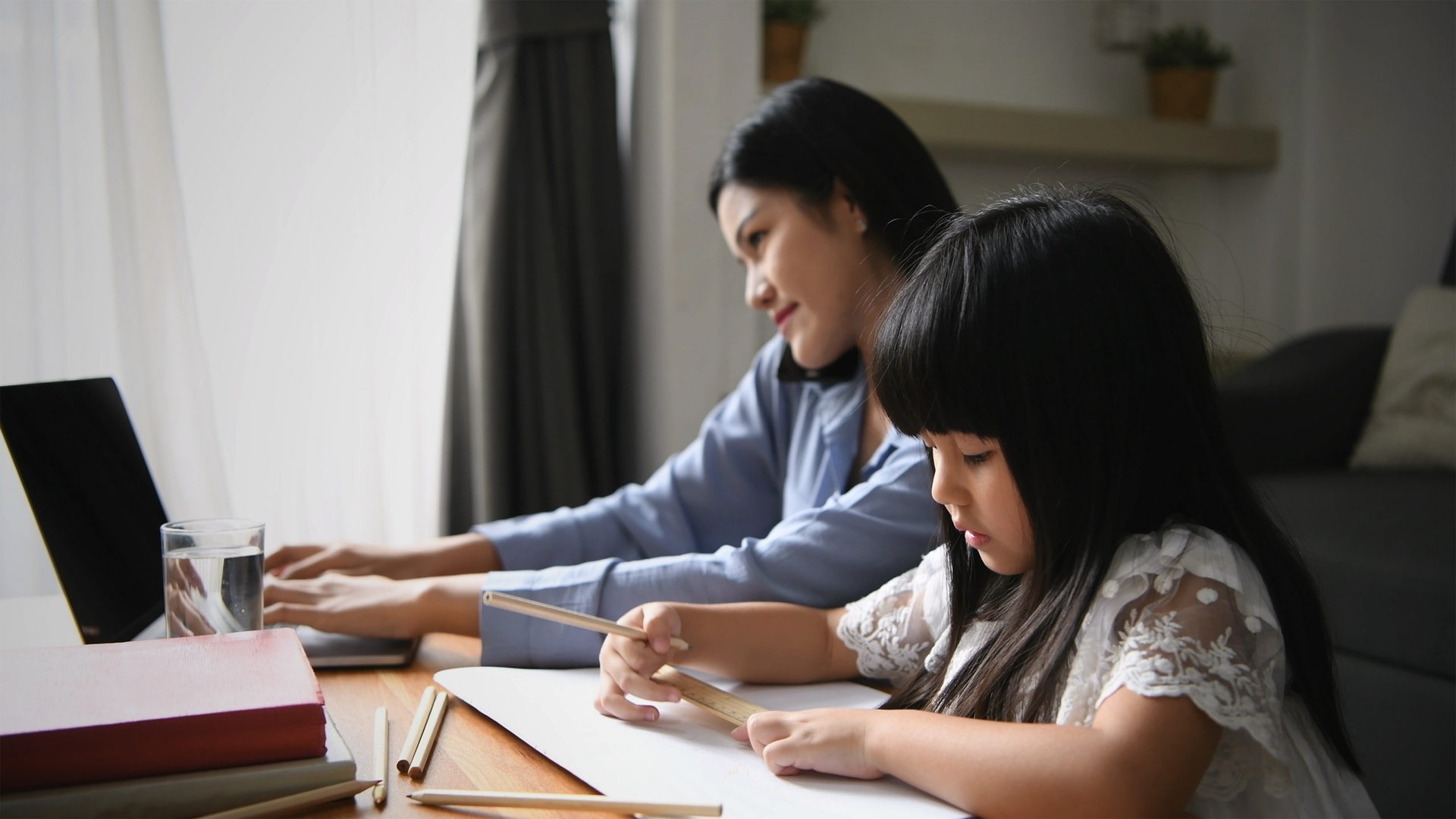 Mom works on a laptop while her child does homework